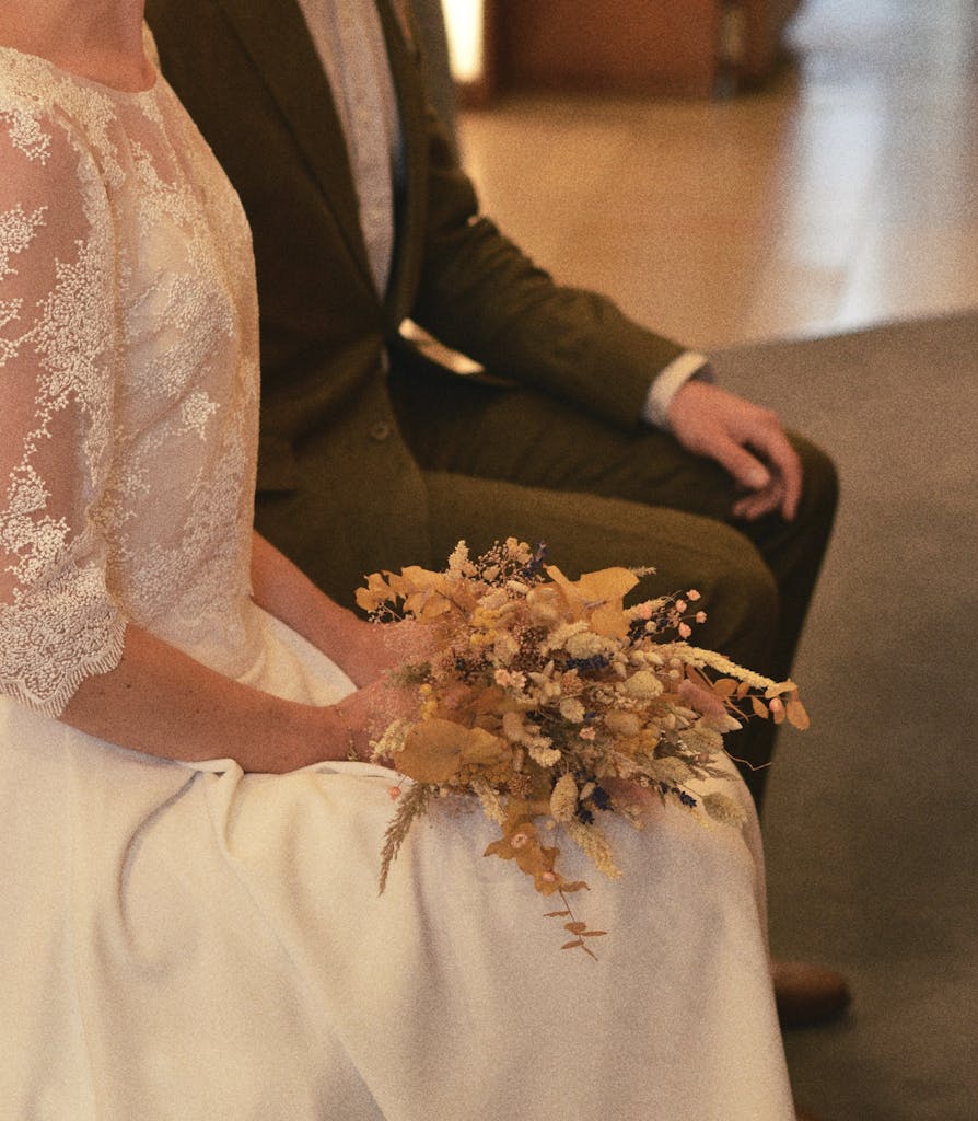 A close-up of a bride holding a bouquet, sitting beside the groom during a wedding ceremony.