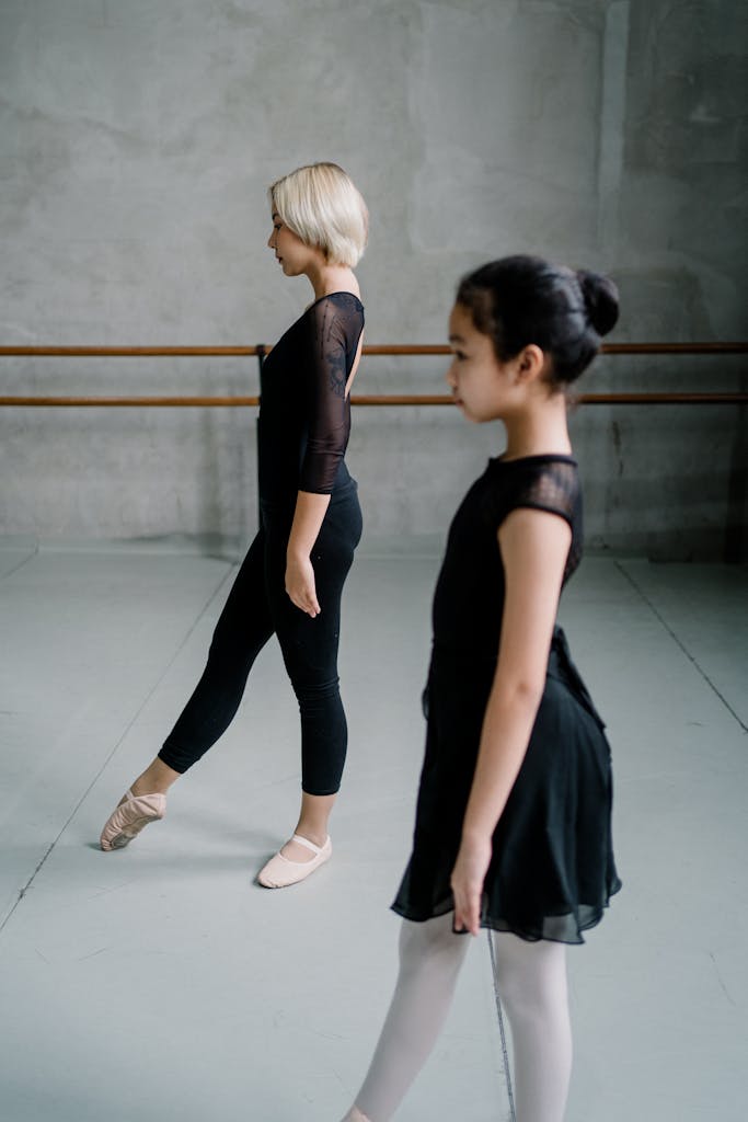 A graceful ballet teacher and student practicing poses in an indoor studio.