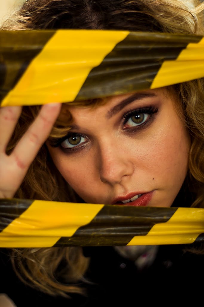 Artistic portrait of a woman peering through bold caution tape.