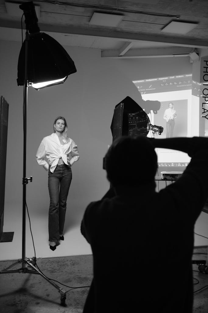 Black and white photo of a studio shoot with a woman posing and photographer capturing the moment.