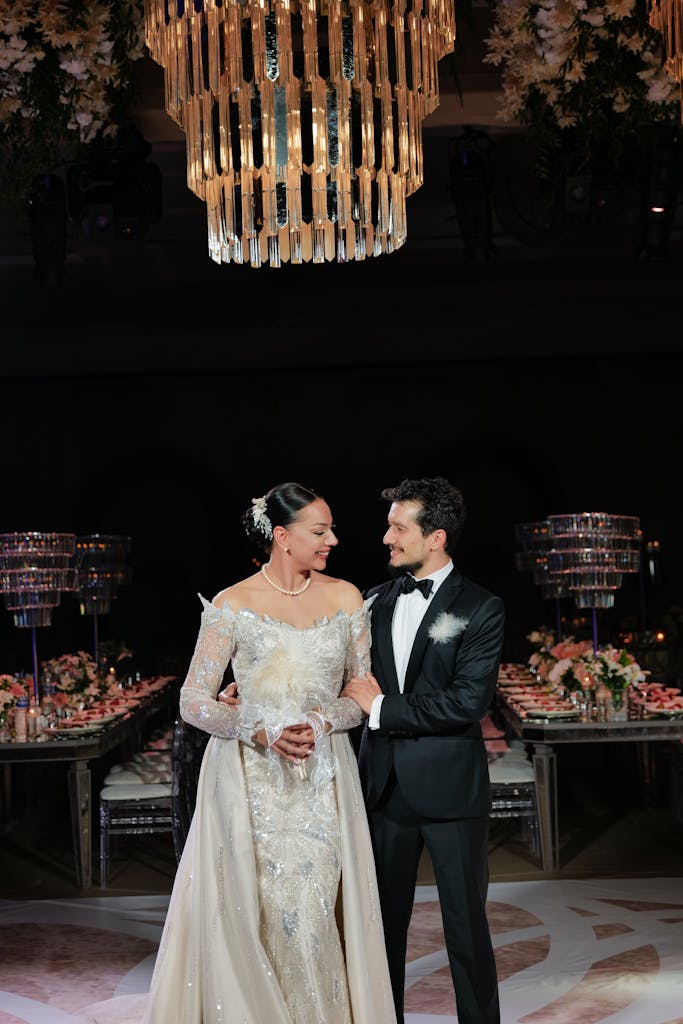 Bride and groom in elegant attire under a stunning chandelier at a wedding reception.