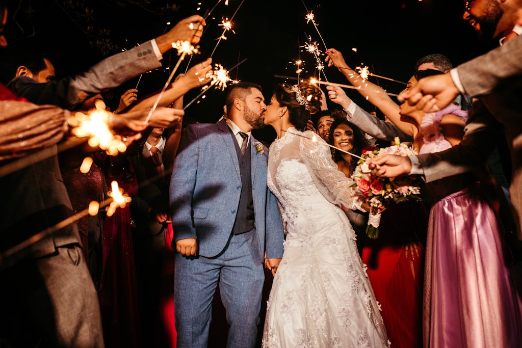 Bride and groom kissing amid sparklers during wedding celebration surrounded by guests.