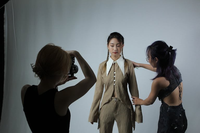 Model preparing for a fashion photoshoot with assistance and photographer.