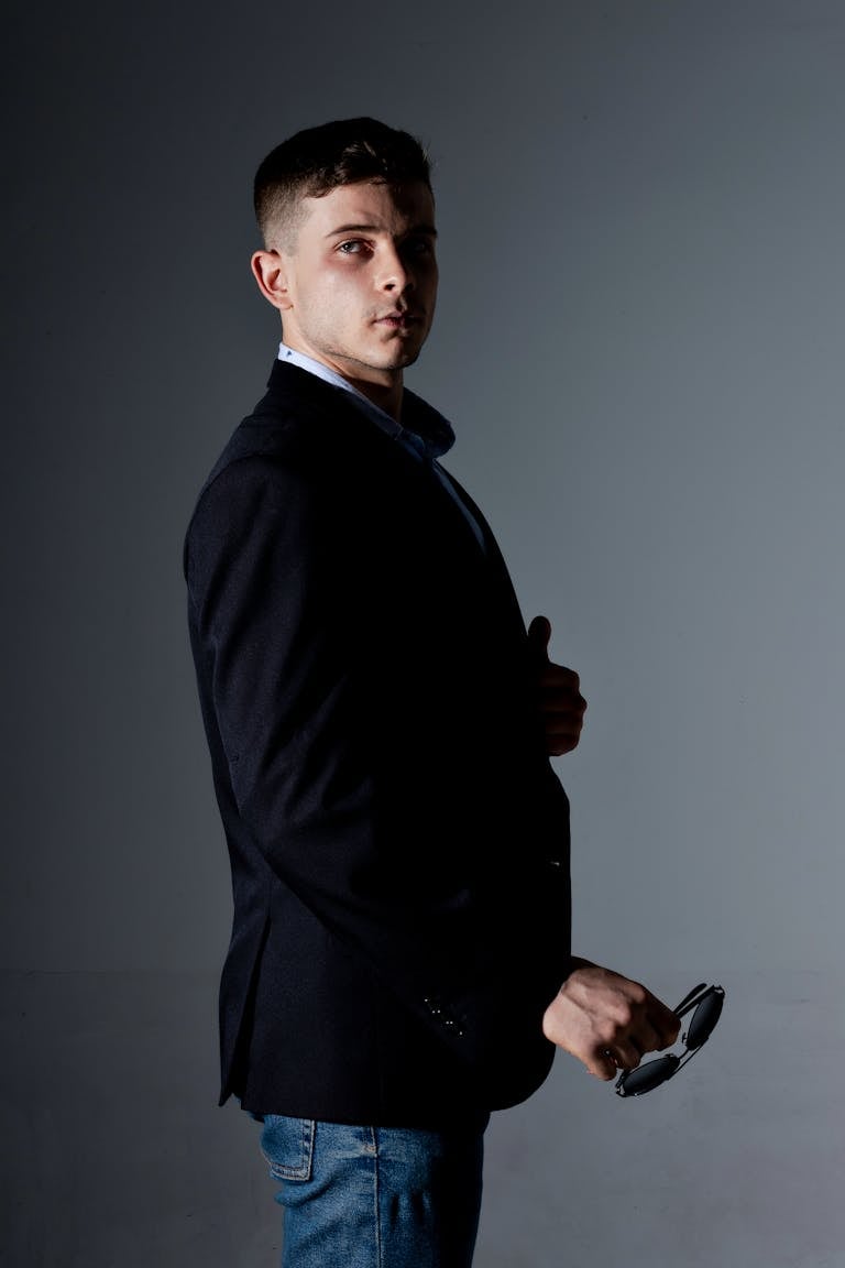 Portrait of a stylish man holding sunglasses in a moody studio setting, Belo Horizonte.