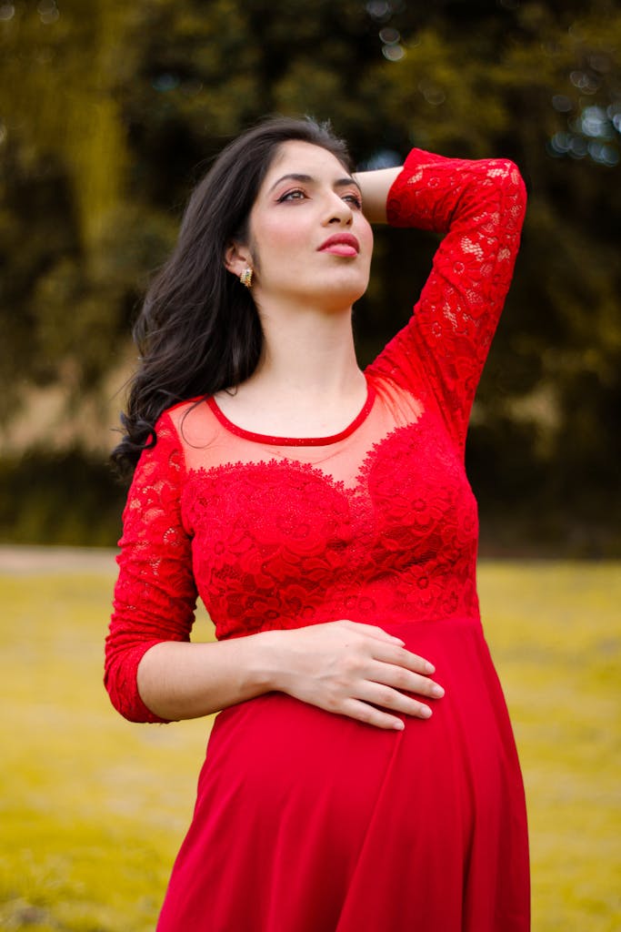 Pregnant woman in a vibrant red dress posing outdoors, exuding elegance and confidence.