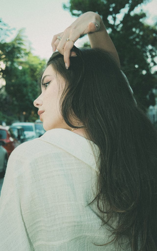Profile of a young woman with long hair in an outdoor setting, exuding elegance.