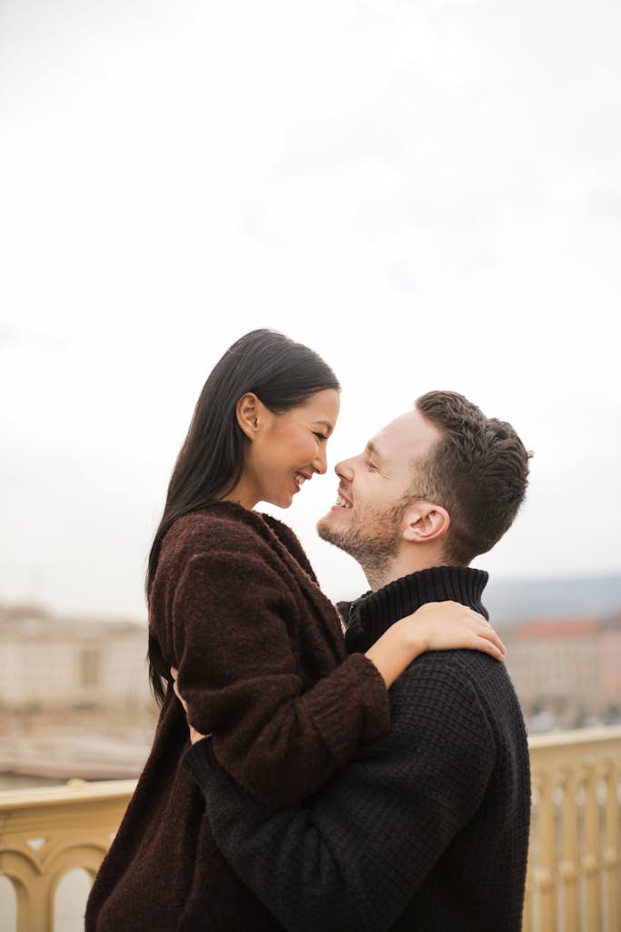 Smiling couple embracing lovingly on a bridge outdoors, exuding romance and joy.