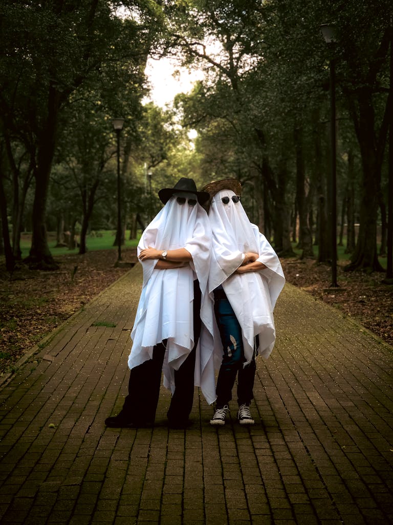 Two people in ghost costumes pose playfully in a wooded park path.