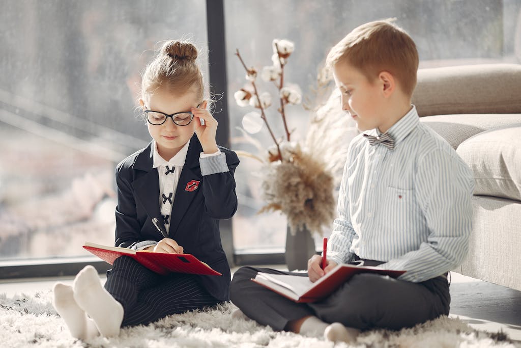 Two young children sit on the floor with notebooks, engaging in a learning activity.