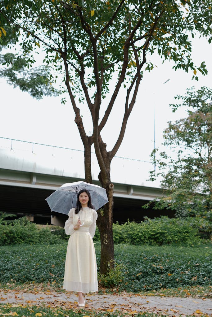 Young woman holding an umbrella standing under a tree in Ho Chi Minh City, Vietnam.